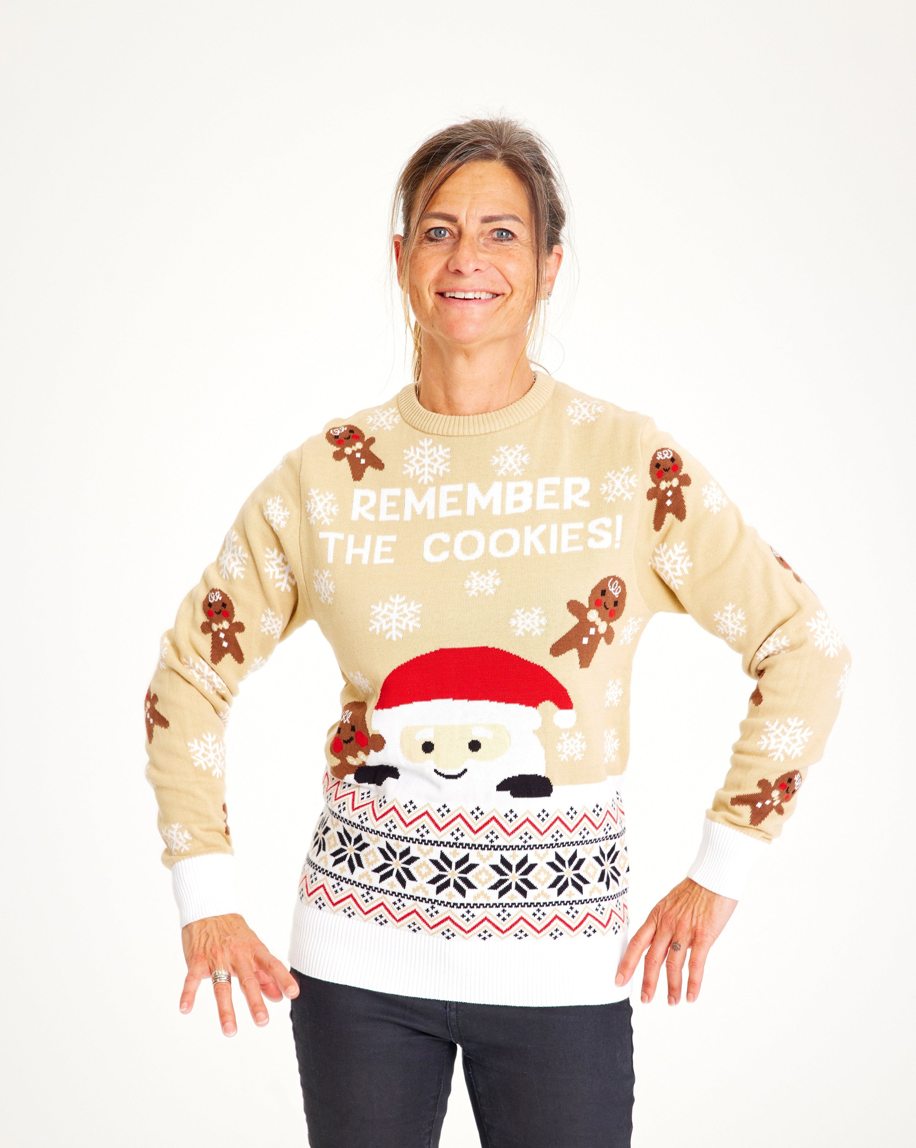 En smilende dame med hænderne i siden er iført en beige julesweater.